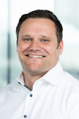 Portrait von Herrn Ermel mit breitem Lächeln und weißem Hemd