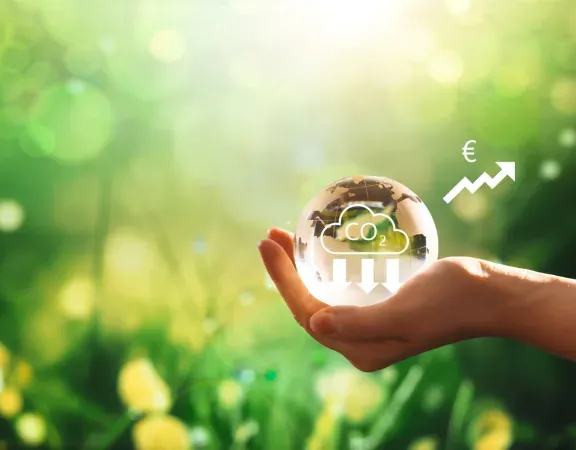 Grüner Grashintergrund mit Hand, die eine Weltkugel hält. CO2 geht runter, der Gewinn langfristig hoch